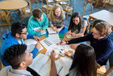 A group of students sit at a table working on a project together
